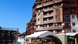 A multi-story wooden building with balconies, likely a hotel or lodge, with a stone base and a snow-covered roof.