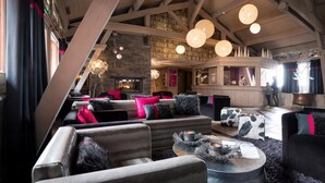 A cozy lounge area with sofas and armchairs, a fireplace, and a bookshelf in the background.