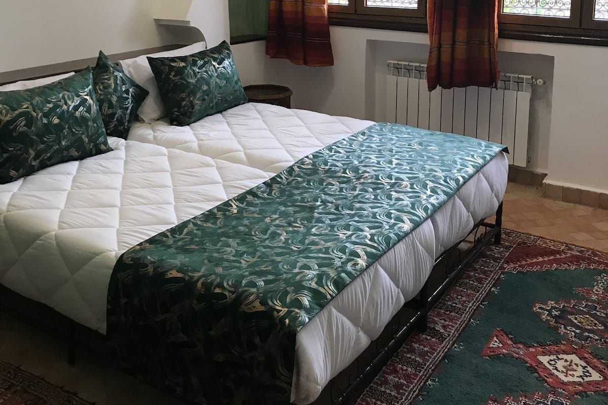 Ein Schlafzimmer mit einem Bett, einem Spiegel und zwei mit Vorhängen versehenen Fenstern.
