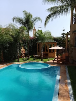 A swimming pool with a curved edge, surrounded by palm trees and a gazebo. - Les Jardins De Ryad Bahia (Ait Ouallal)