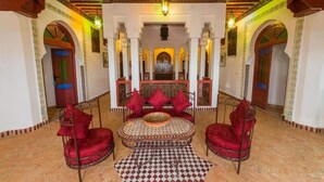 Ein traditionelles marokkanisches Interieur mit einer zentralen Sitzecke, verzierten Bögen und einem Fußboden mit Muster.