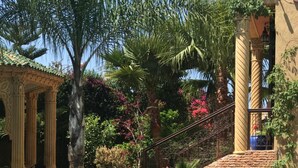 Ein Poolbereich mit einer Pergola, Palmen und einer Backsteinmauer.
