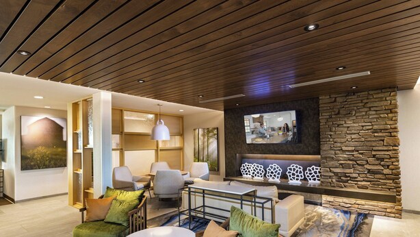 Een moderne woonkamer met een accentmuur van steen, een flatscreen televisie en een zithoek met groene en beige banken.