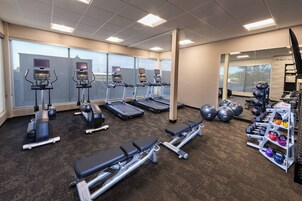Un gimnasio con cintas de correr, elípticas, una prensa de banca y una barra de mancuernas.