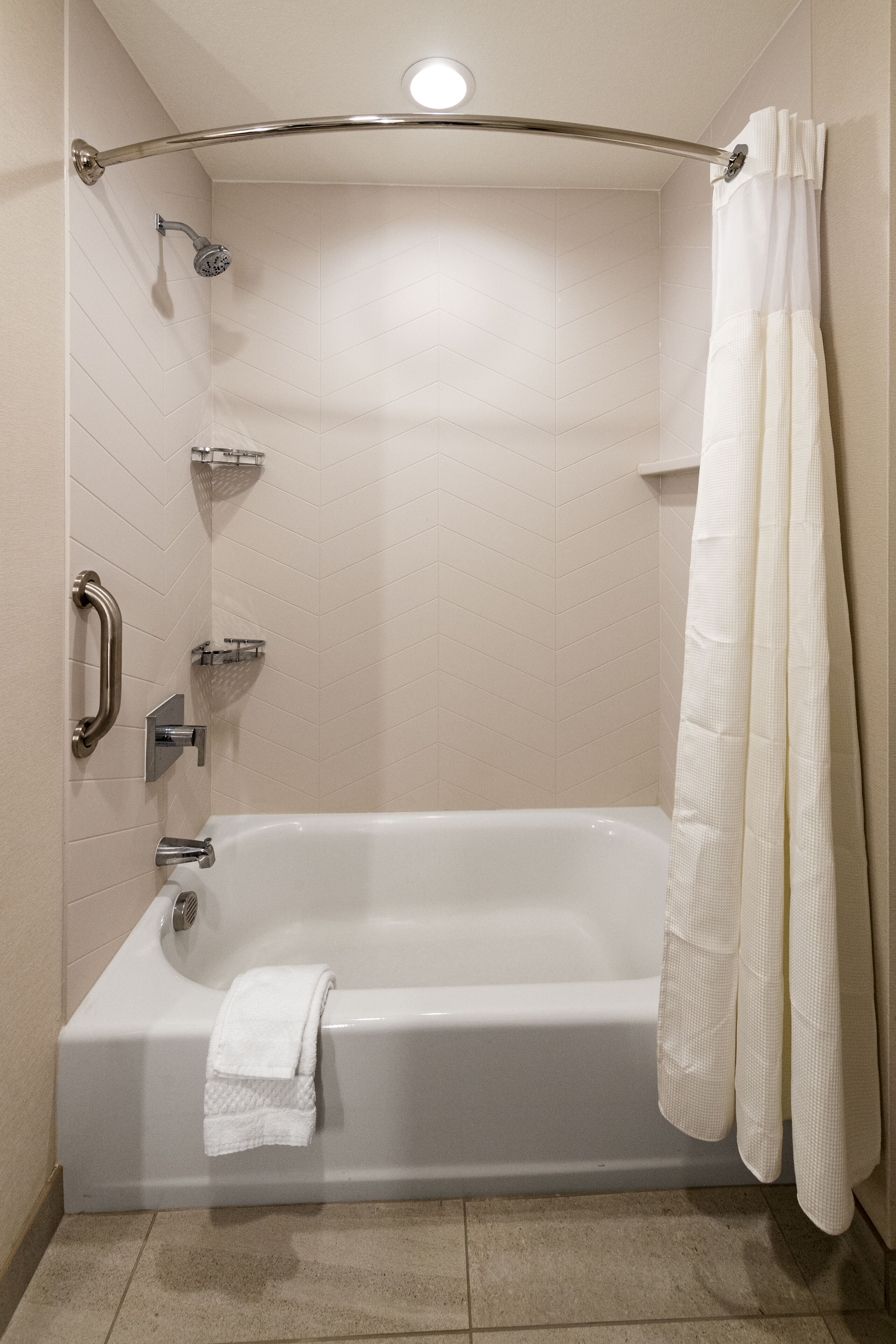 A modern bathroom with a walk-in shower, grab bars, a handheld showerhead, and a white bathtub with a towel.