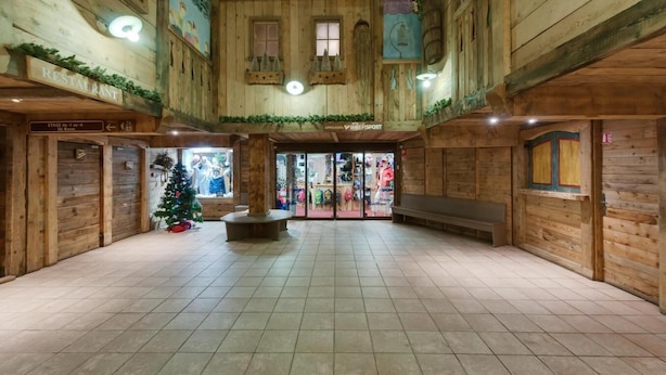 Ruime binnenzone met houten wanden en betegelde vloer, met kerstboom, banken en een bordje voor de skiopslag.