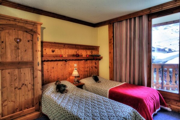 A room with two beds, wooden headboard, a lamp, and a view of a snowy landscape through a window.