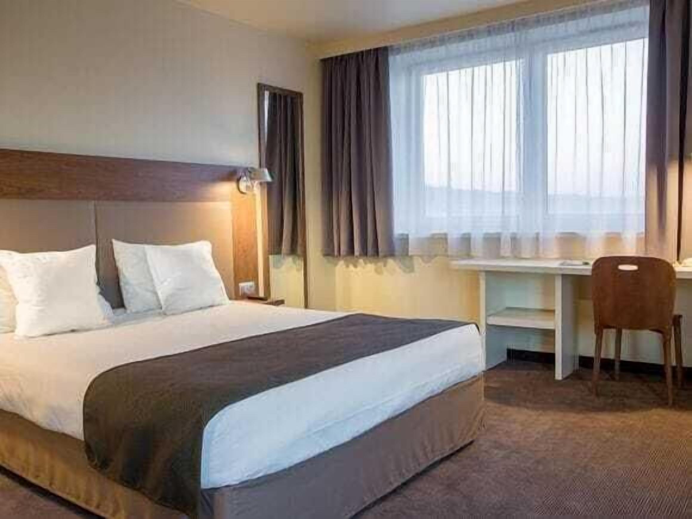 A hotel room with a bed, a desk, and a chair.