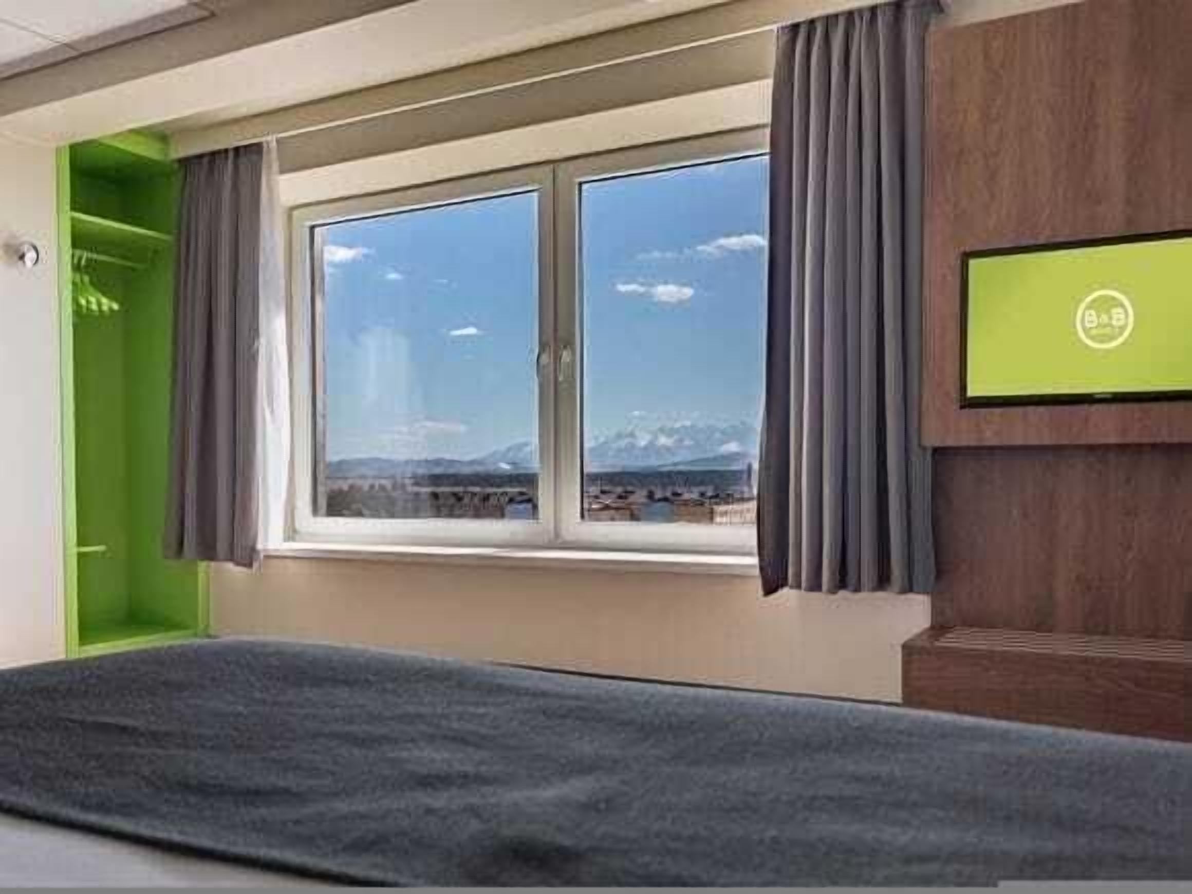 A hotel room with a bed, a window with a view of mountains, a green wall, and a television on the wall.