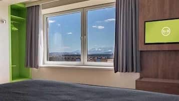 A hotel room with a bed, a window with a view of mountains, a green wall, and a television on the wall.