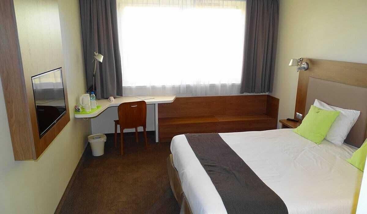 A hotel room with a bed, a desk, a chair, a TV, and a window with curtains.