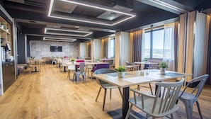 Un espace repas moderne avec un plancher en bois, de nombreuses tables et chaises, et de grandes fenêtres dotées de rideaux.