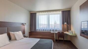 Habitación de hotel con cama, escritorio, silla, televisión y ventana con cortinas.