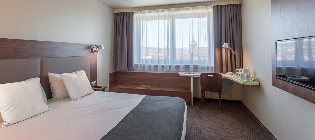 A hotel room with a bed, a desk, a chair, a TV, and a window with curtains.