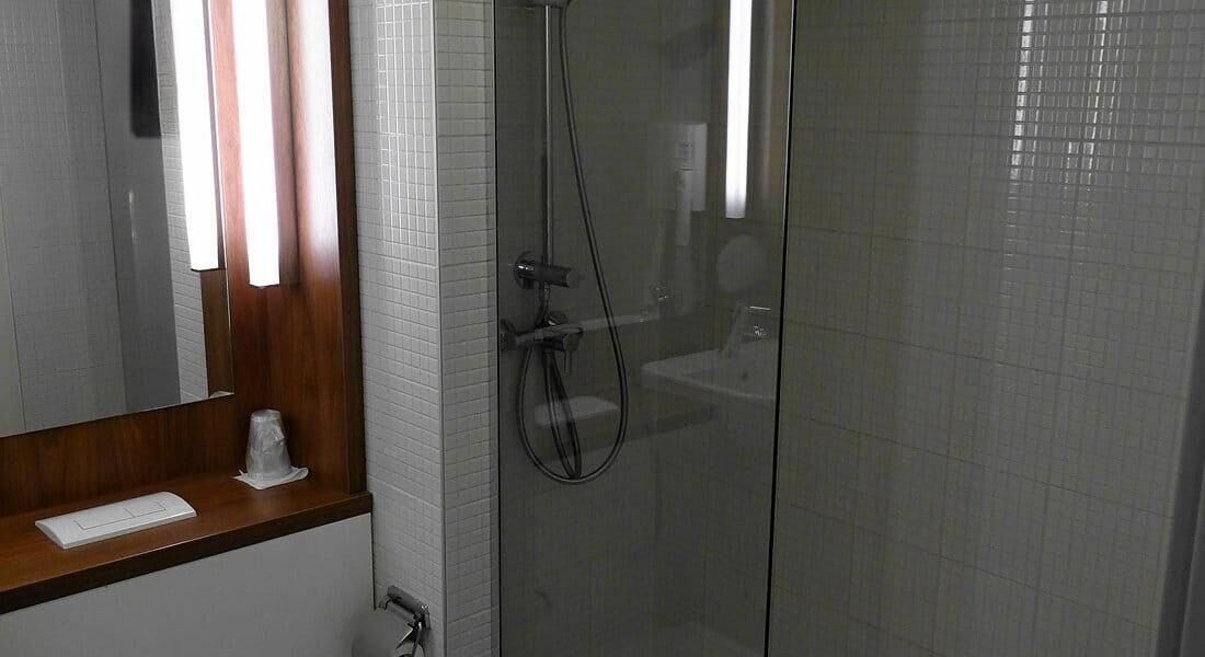 Un baño con cabina de ducha de vidrio, tocador de madera con espejo y pared cubierta de azulejos blancos.