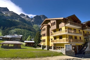 Een hotel met meerdere verdiepingen, balkons, een stenen trap en een berg op de achtergrond.