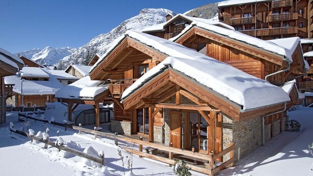 A wooden chalet-style hotel with multiple balconies and large windows, surrounded by snow-covered mountains. - Chalet, 50m from resort center, swimming pool, sauna, balcony, fireplace or stove, parking, tv (Les Deux Alpes)
