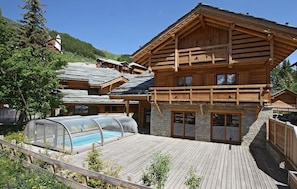 Una cabaña de madera con piscina, paredes de piedra y terraza de madera.