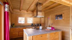 A wooden cabin kitchen with a central island, wooden cabinets, a microwave, and a stove. - Chalet, 50m from resort center, swimming pool, sauna, balcony, fireplace or stove, parking, tv (Les Deux Alpes)