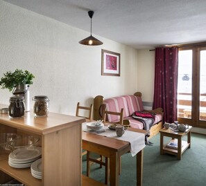 A cozy room with a wooden dining table, a bed with a striped blanket, a window with curtains, and a hanging light fixture. - 100m from resort center, balcony, tv, ski locker, 33m², Val Thorens (Val Thorens)