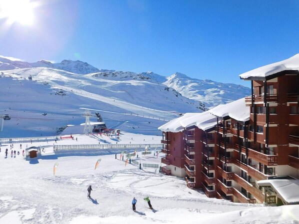 Un centro de esquí con un edificio de varios pisos, pistas de esquí y una montaña al fondo.
