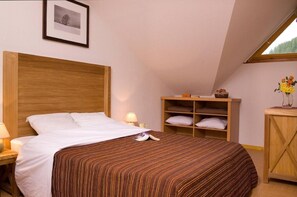 A bedroom with a wooden headboard, a bed with white linens, a bedside table with a lamp, a wooden nightstand, a shelf with folded linens, and a window with a view of trees. - Wifi, 50m from shops, view ski slopes, swimming pool, balcony, 28-29m², Les Orres (Les Orres)