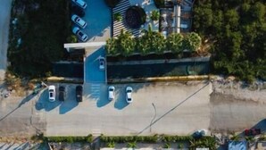 Vista aérea de una propiedad frente a la playa con piscina, sombrillas y un edificio de techo plano.