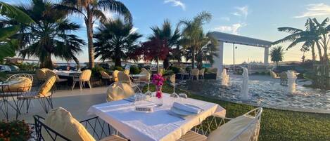 An outdoor dining area with tables and chairs, a water feature, and palm trees.
