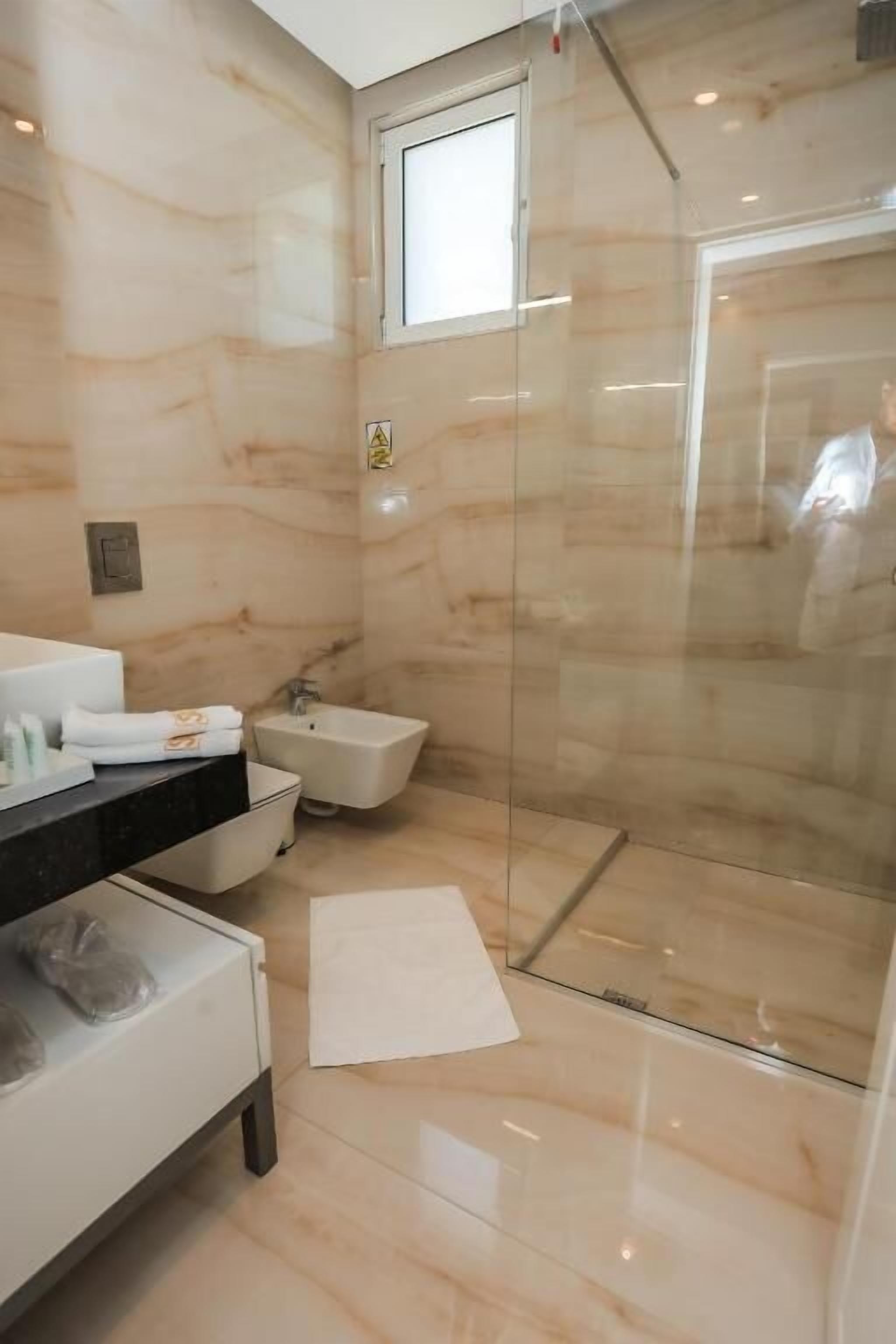Une salle de bain moderne avec une douche à parois de verre, un meuble-lavabo doté d’un plan de travail noir et un mur en marbre.