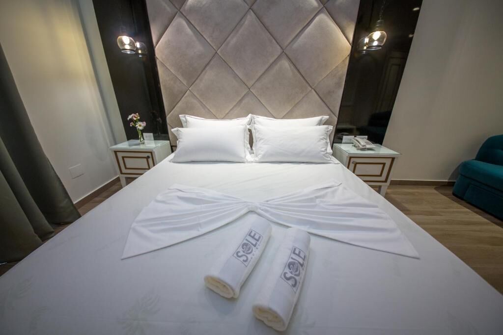 A hotel room with a large bed, two bedside tables, and a headboard with a diamond pattern.