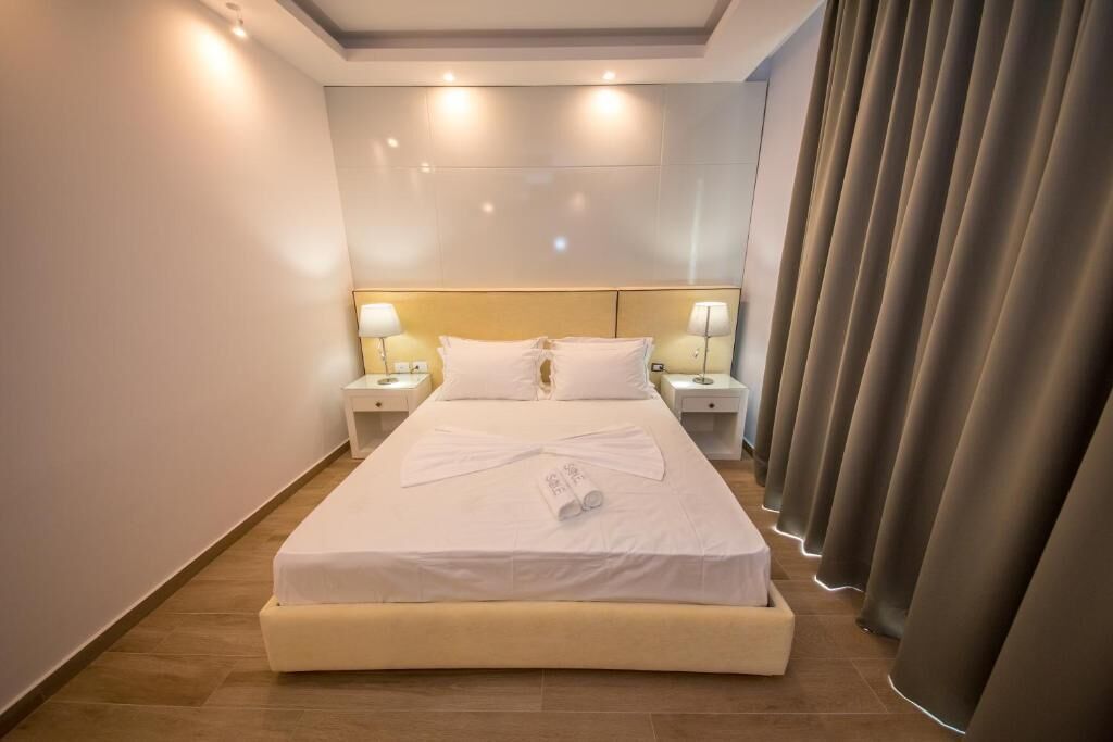 A hotel room with a large bed, two bedside tables with lamps, a headboard, and a curtain.