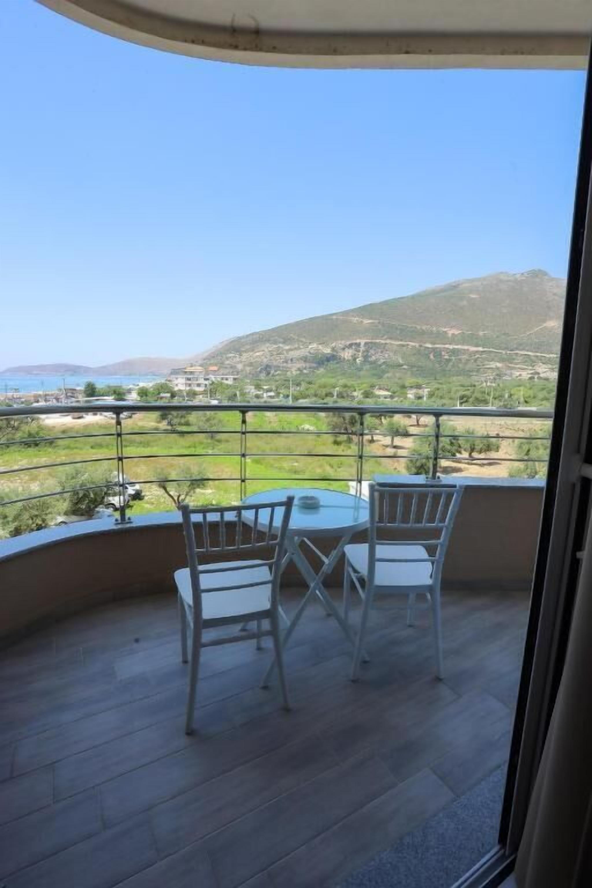 A balcony with two white chairs and a table, overlooking a scenic landscape with hills and a body of water.