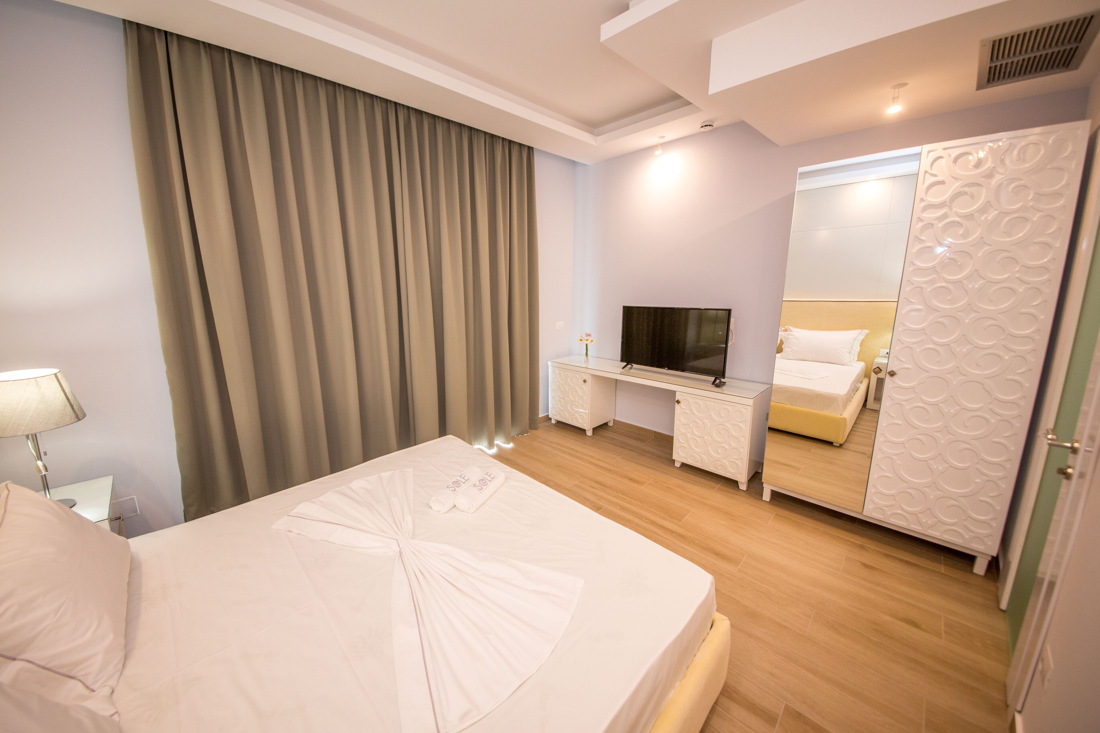 A hotel room with a bed, a TV, a desk, a wardrobe, and a mirror.