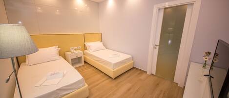 A hotel room with two beds, a nightstand, a lamp, a TV, and a door.