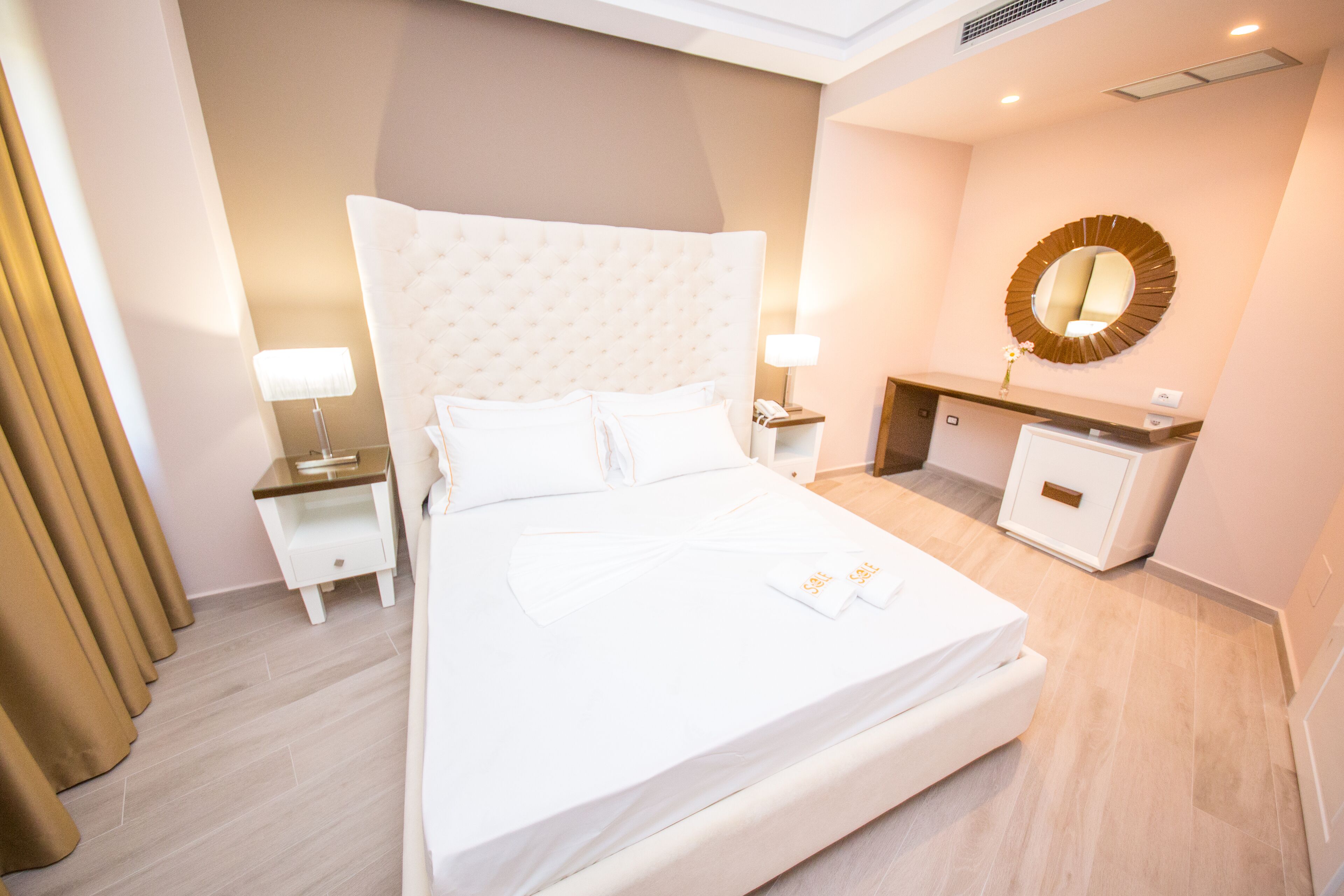 A hotel room with a large bed, bedside tables, a desk, a mirror, and a small cabinet.
