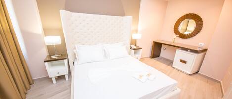 A hotel room with a large bed, bedside tables, a desk, a mirror, and a small cabinet.