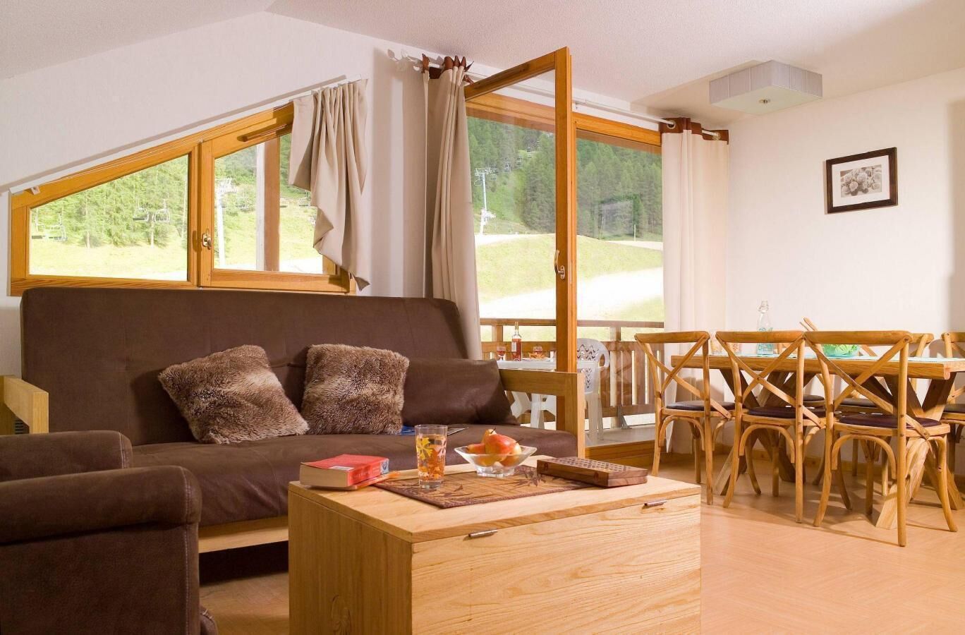 A cozy living room with a sofa, a wooden coffee table, and a dining area with wooden chairs.