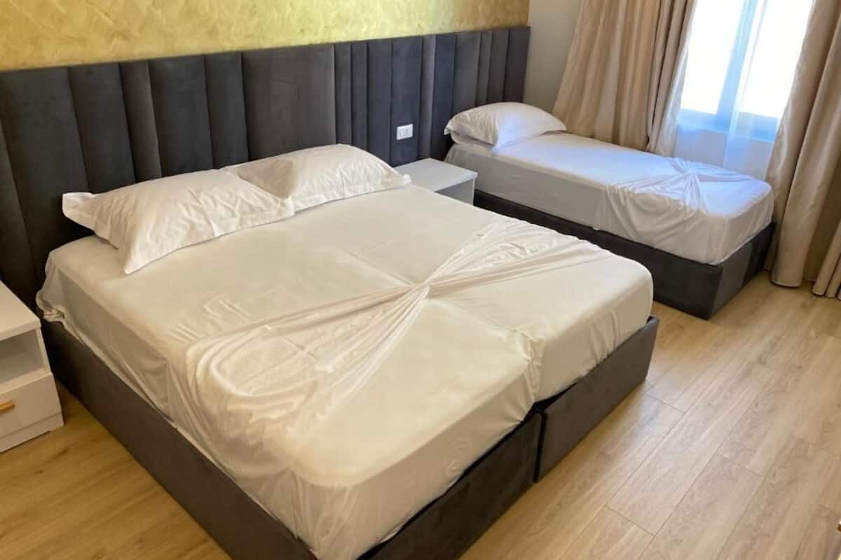 A hotel room with two beds, a headboard, a bedside table, and a window with curtains.