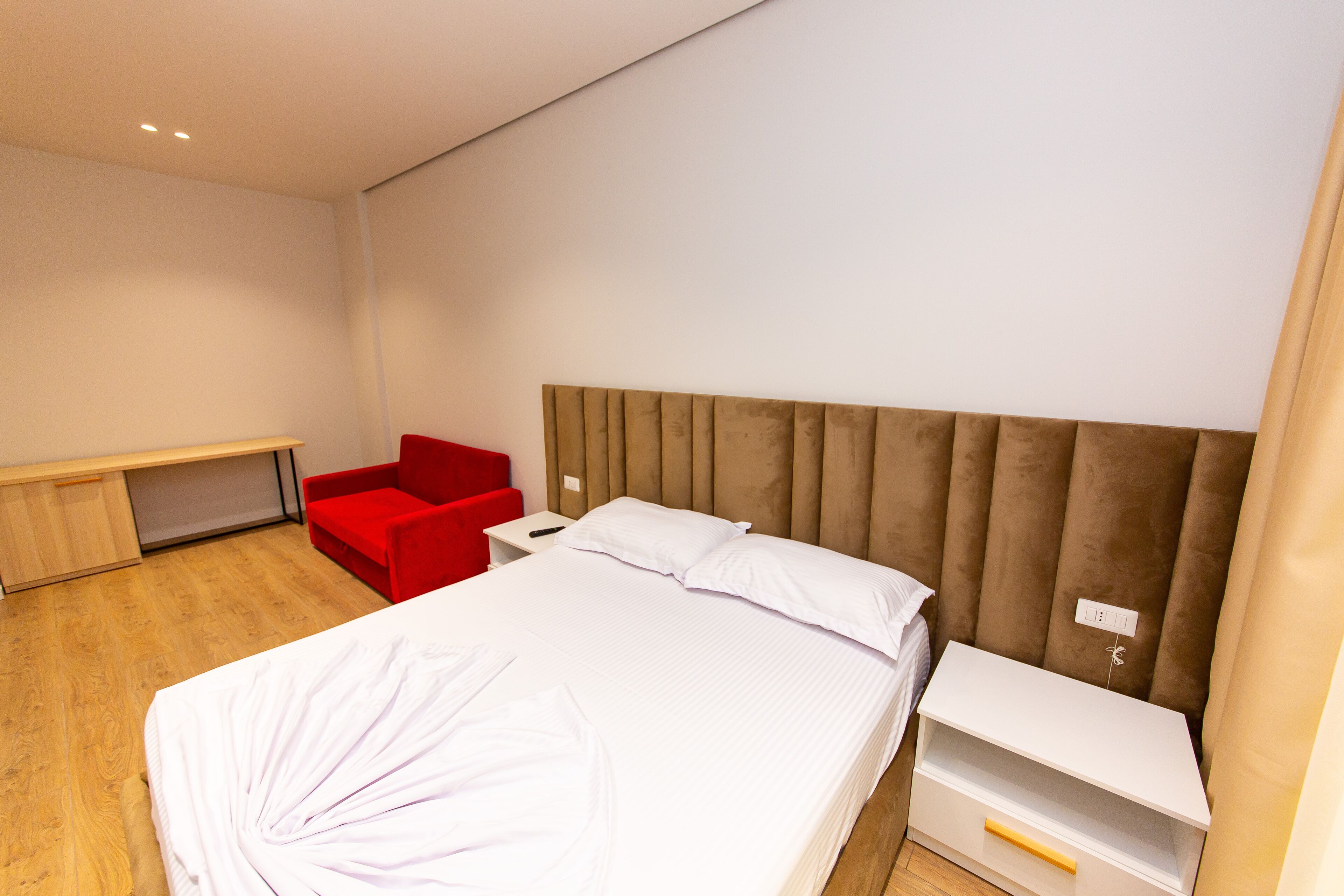 Een moderne hotelkamer met een groot bed, een rode stoel, een bureau en een witte nachtkastje.