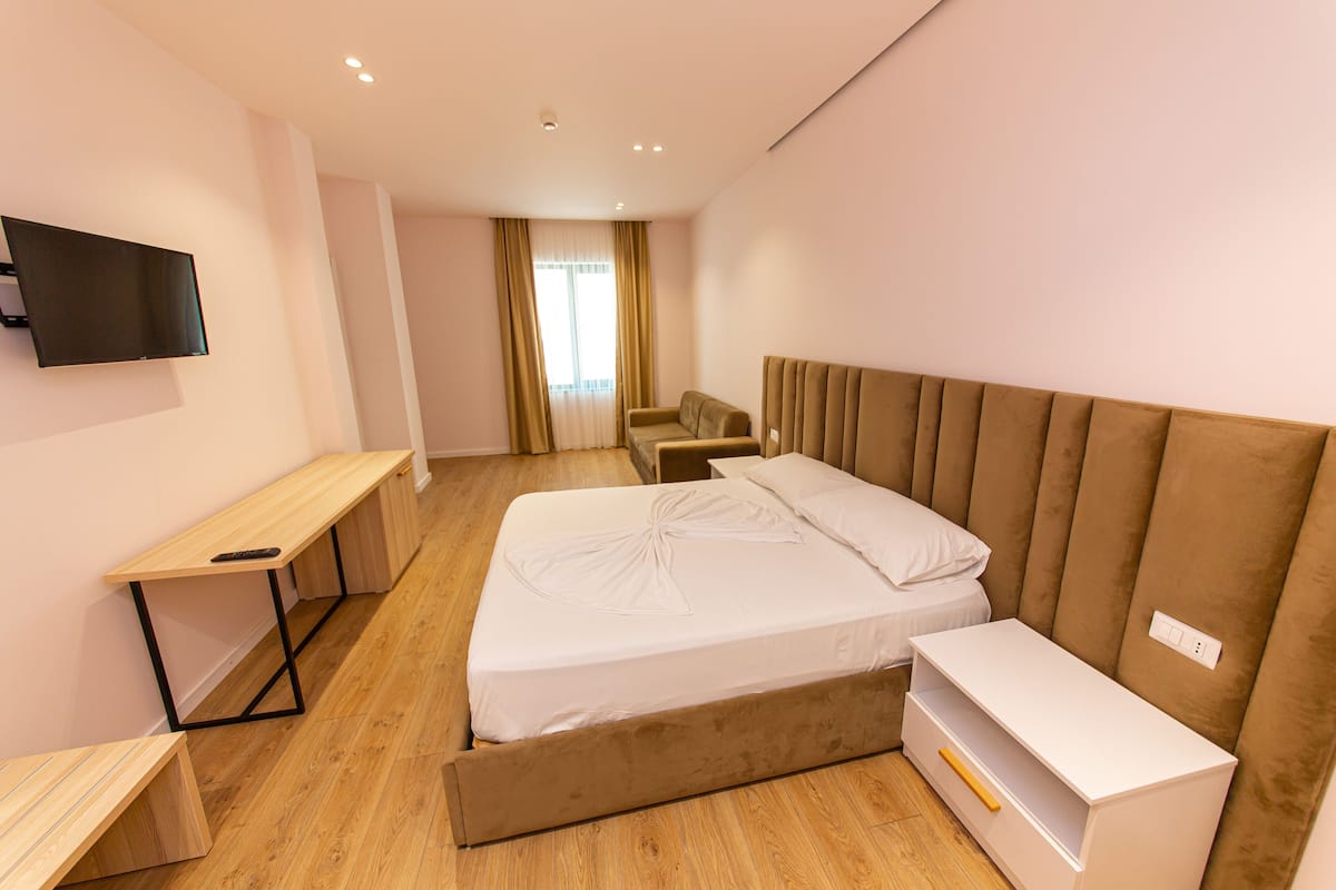 A modern hotel room with a bed, a desk, a chair, and a TV mounted on the wall.