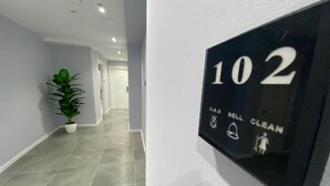 A hallway with a potted plant, a wall-mounted sign indicating room number 102, and a clean symbol. - Hotel Alion (Durrës)
