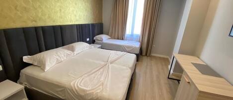 Una habitación de hotel moderna con dos camas, un escritorio de madera y un amplio ventanal con cortinas.