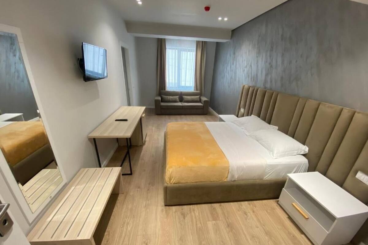 A modern hotel room with a bed, bedside tables, a seating area, and a TV.