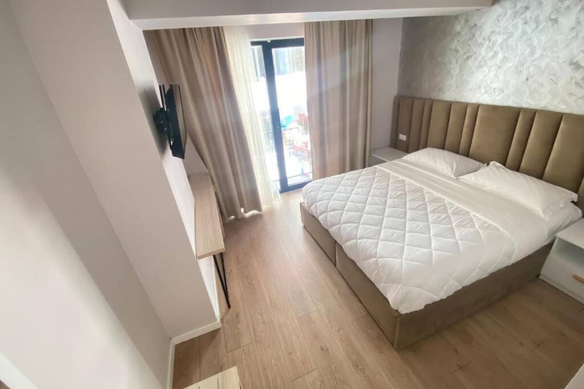 A bedroom with a large bed, a TV mounted on the wall, and a sliding glass door leading to an outdoor area.