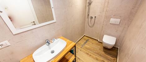 A bathroom with a wooden vanity, a white sink, a mirror, a shower, and a toilet.
