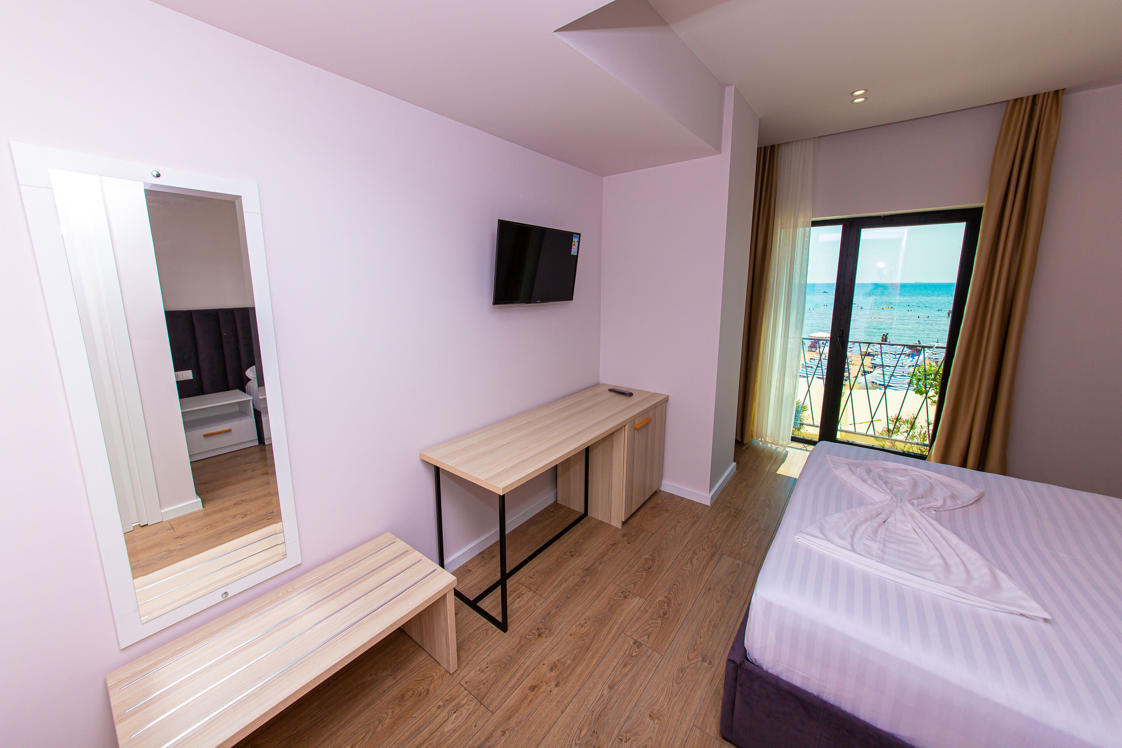 A bedroom with a bed, a desk, a TV, and a balcony with a view of the sea.