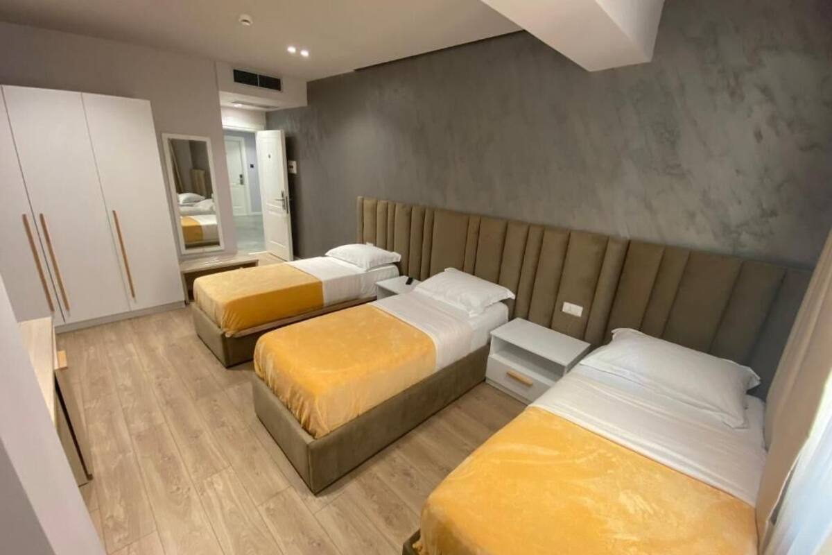 A modern hotel room with three single beds, a wardrobe, and a mirror.