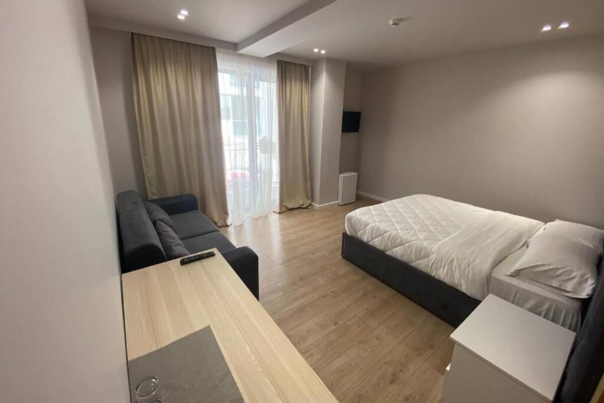 A modern hotel room with a bed, a sofa, a desk, and a TV.