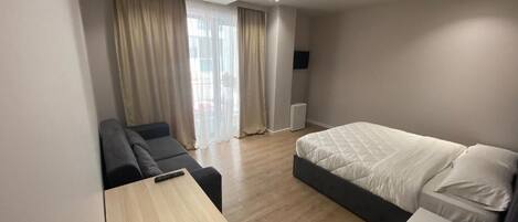 A modern hotel room with a bed, a sofa, a desk, and a TV.