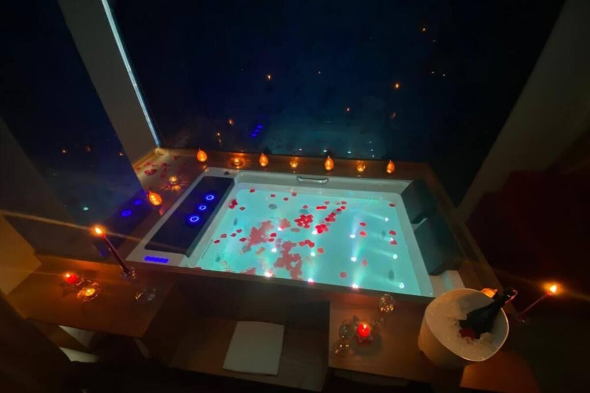 A dimly lit room with a large bathtub filled with rose petals and candles.